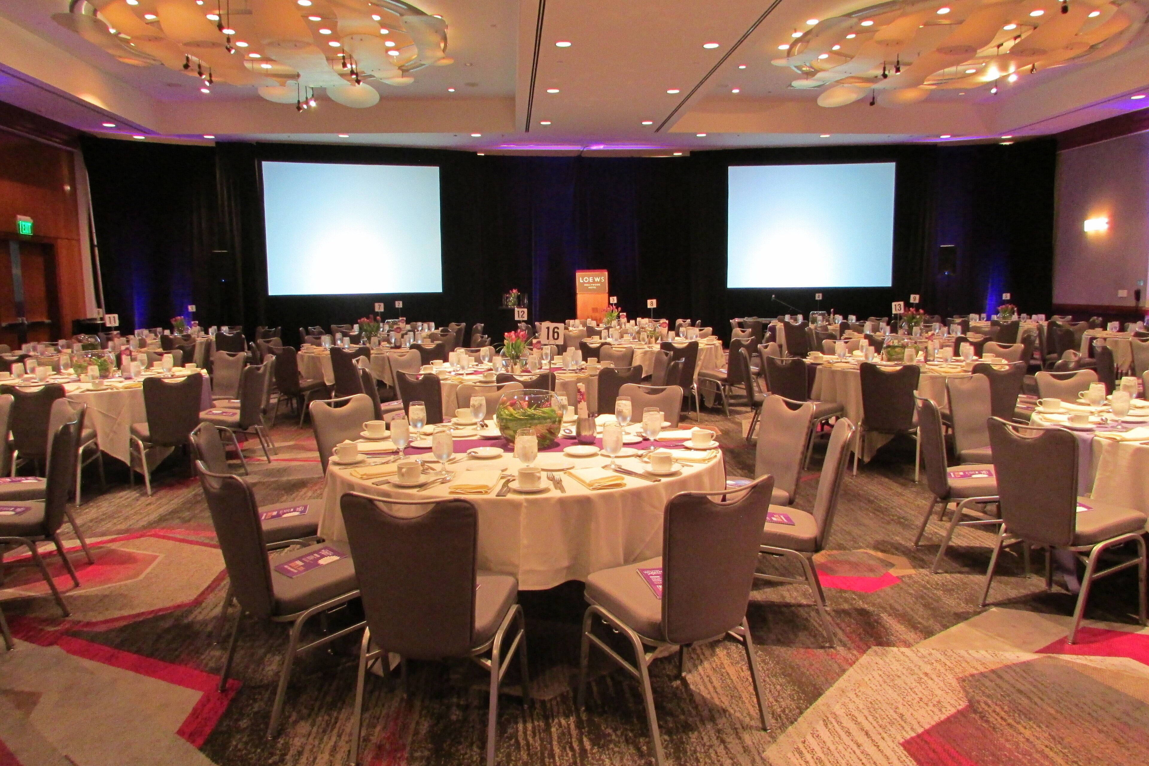 A conference room with round tables, chairs, and a stage with a screen.