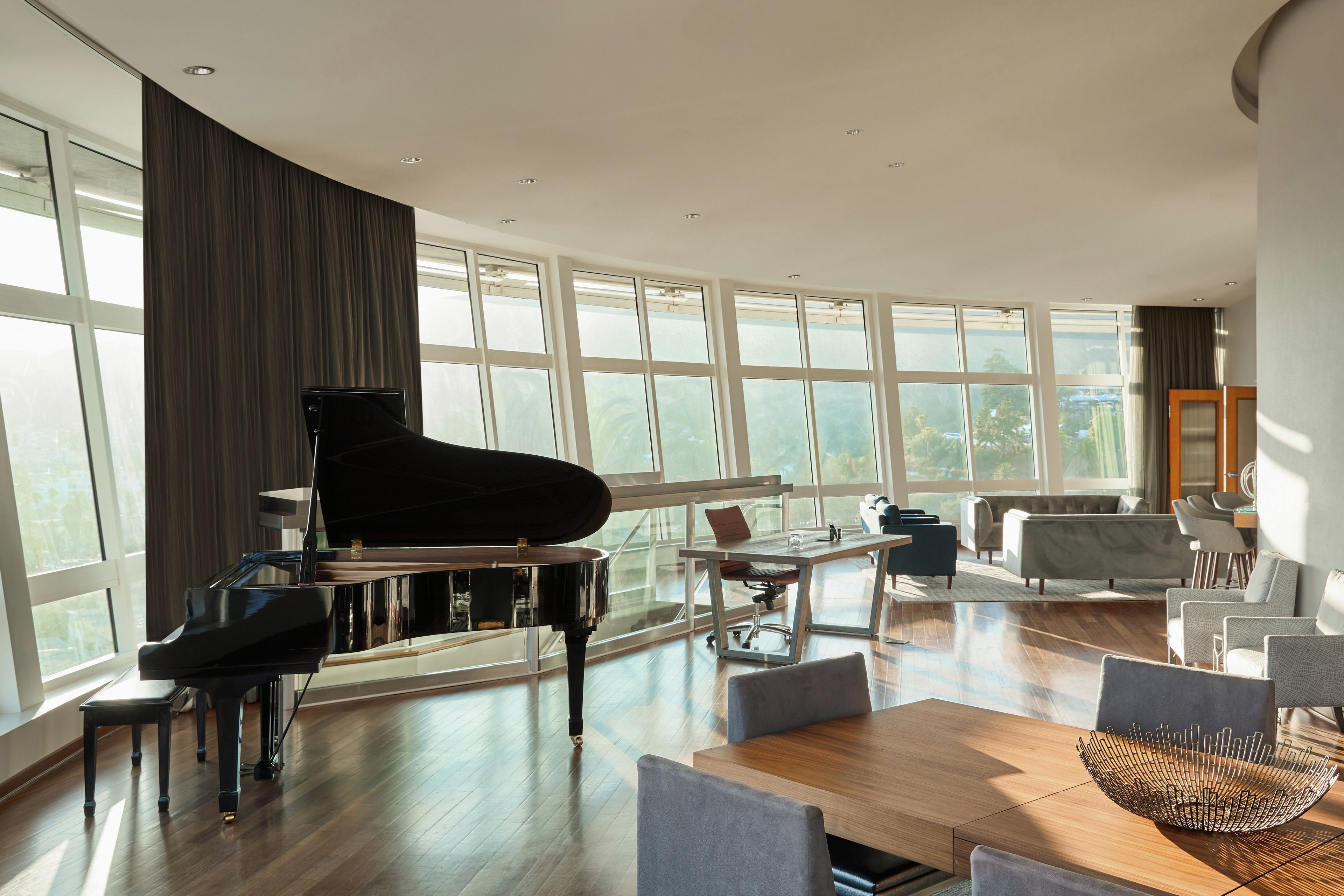 A spacious living room with a grand piano, modern furniture, and large windows offering a view of the outdoors.
