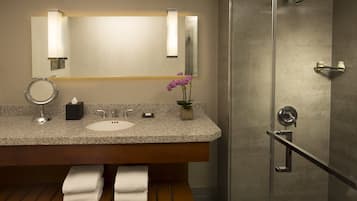 A modern bathroom with a granite countertop, a sink, a mirror, a towel rack, and a shower area.