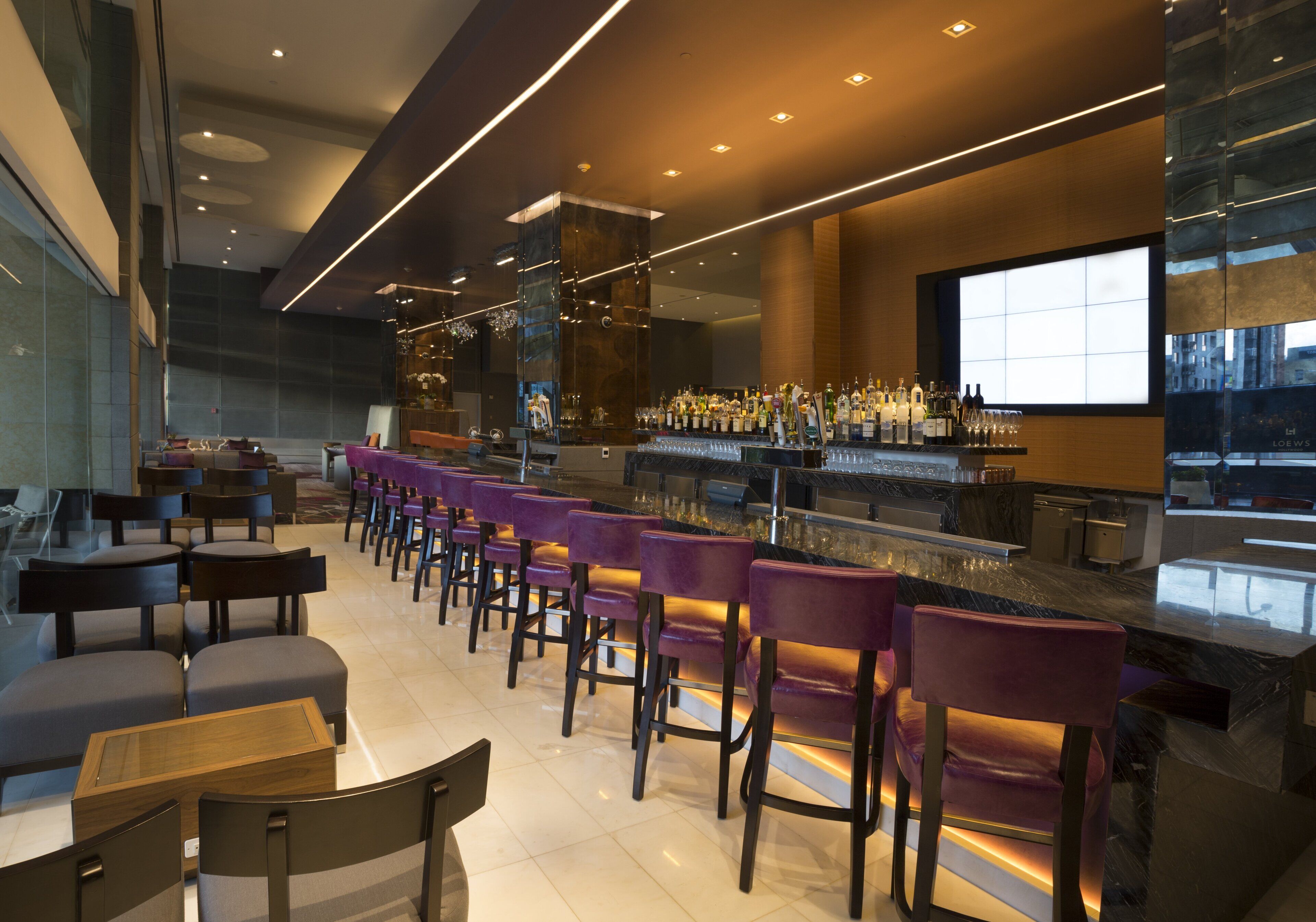 A modern bar area with a long counter, multiple bar stools, and a variety of bottles and glasses.
