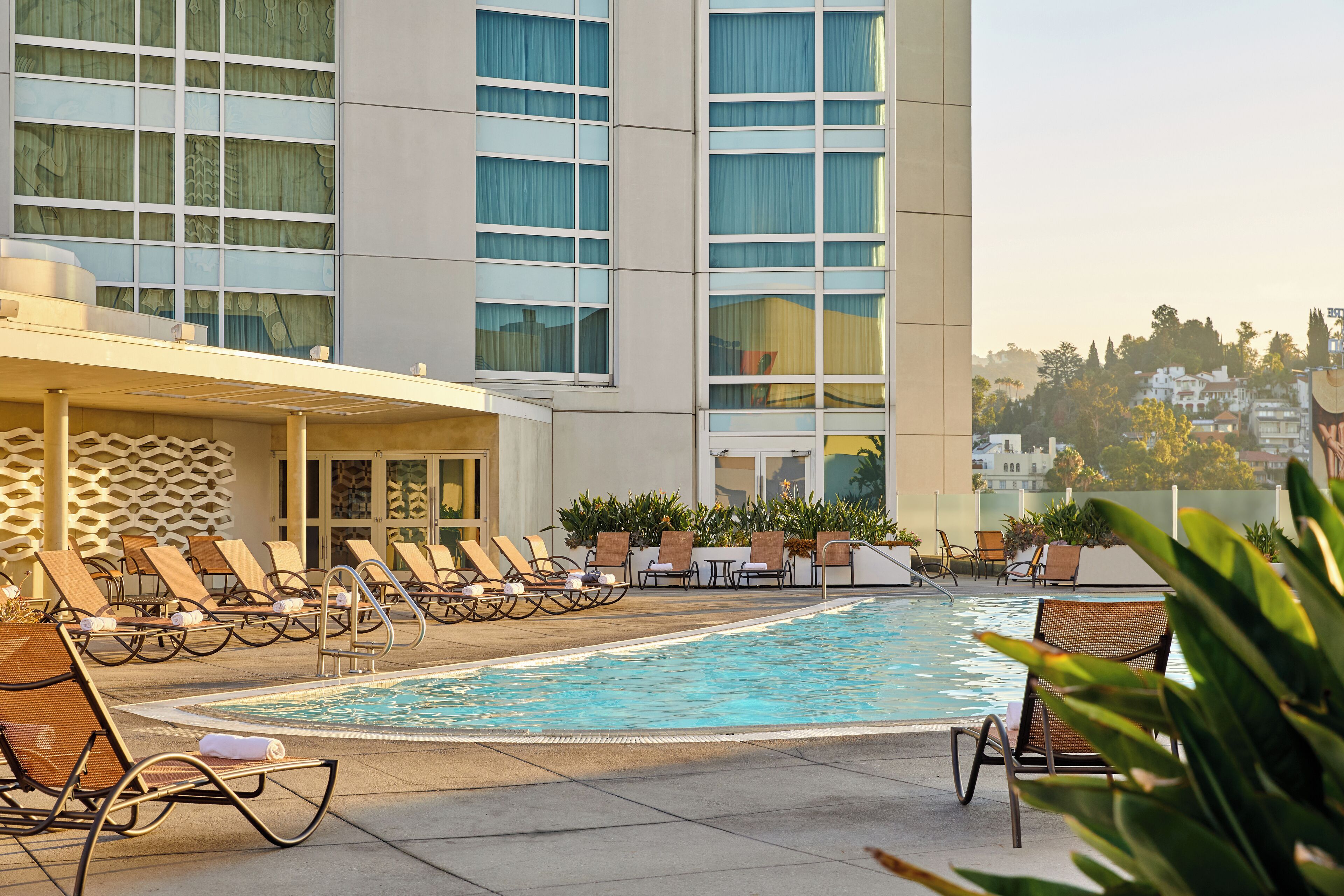 A hotel pool area with lounge chairs and a building with large windows.