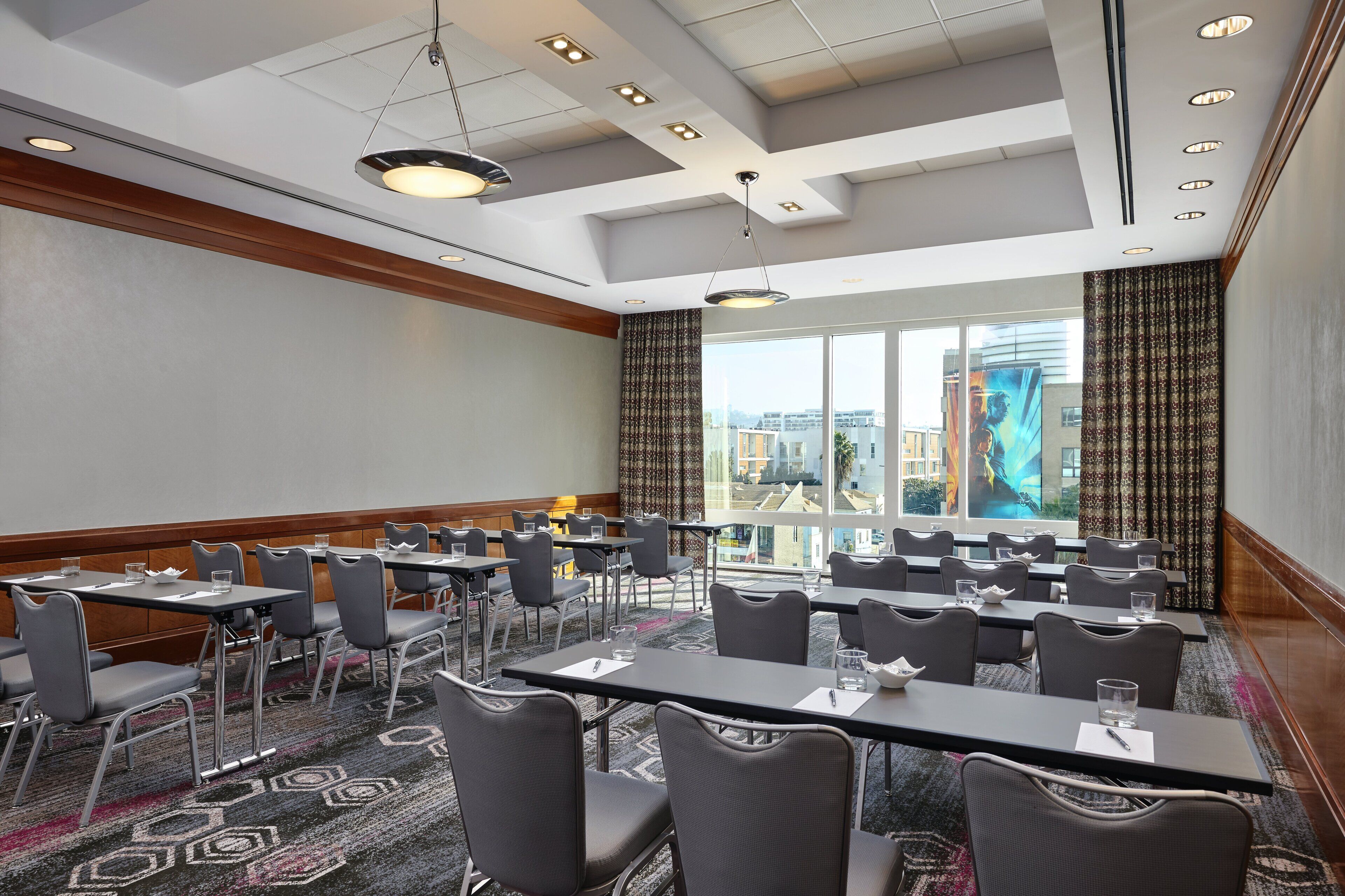 A conference room with tables and chairs, large windows with curtains, and a city view.