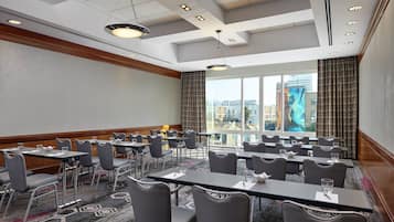 A conference room with tables and chairs, large windows with curtains, and a city view.
