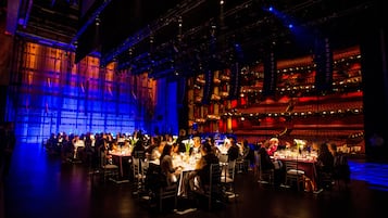 Un amplio comedor interior con numerosas mesas y sillas, techos altos y un escenario con iluminación.