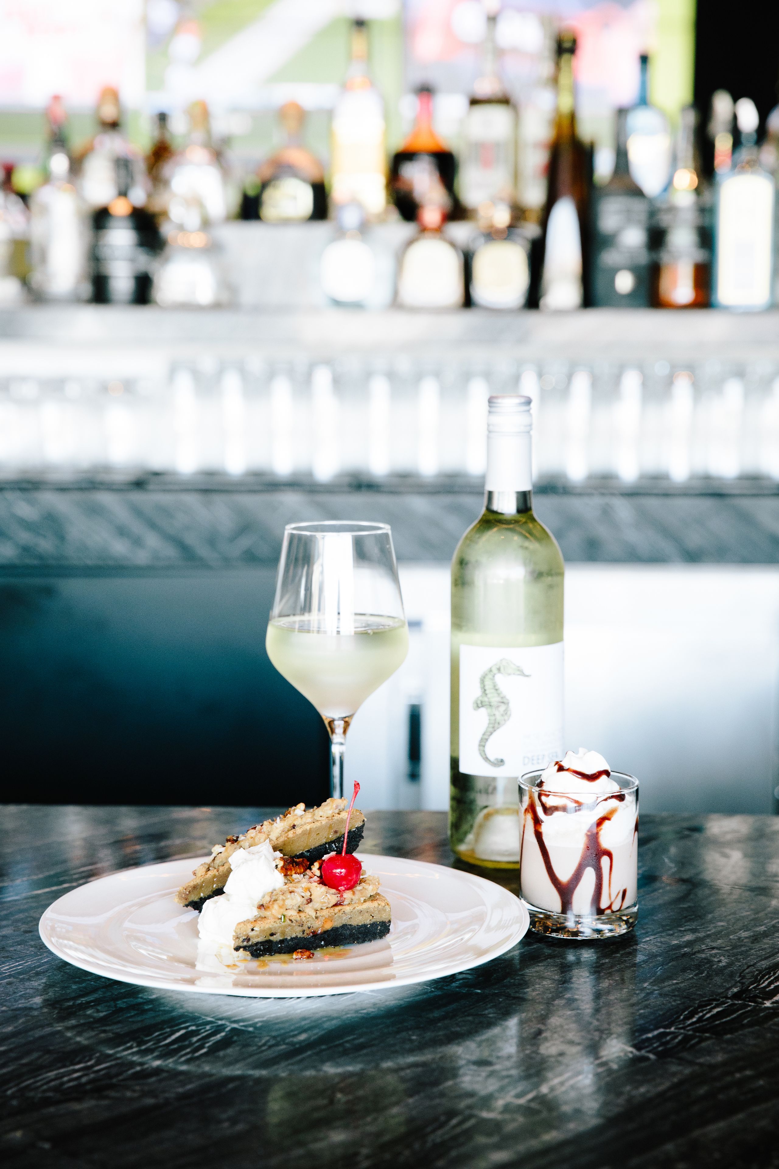 A dessert plate with a slice of pie, a glass of white wine, and a small dessert glass with chocolate sauce and whipped cream.