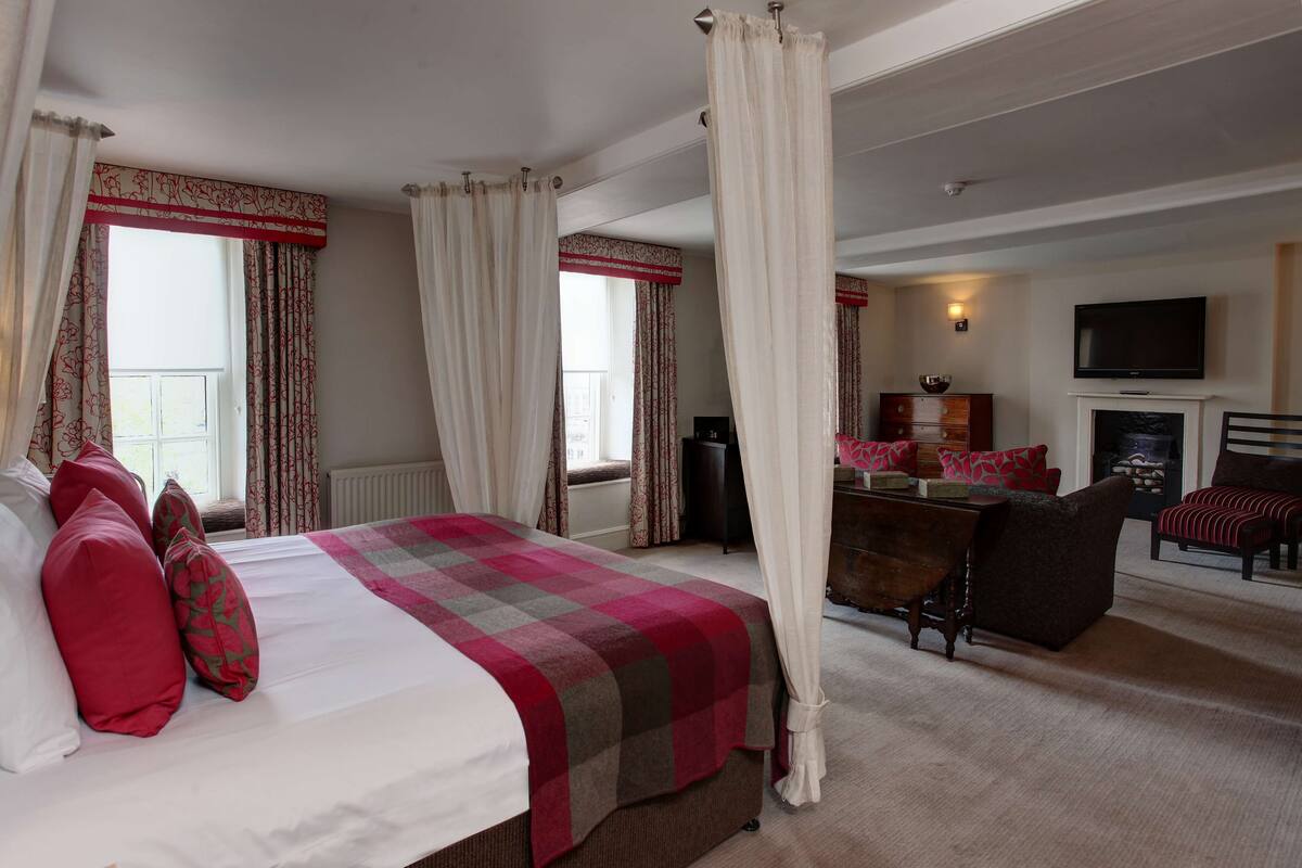 A bedroom with a bed, curtains, a television, a fireplace, and a seating area.