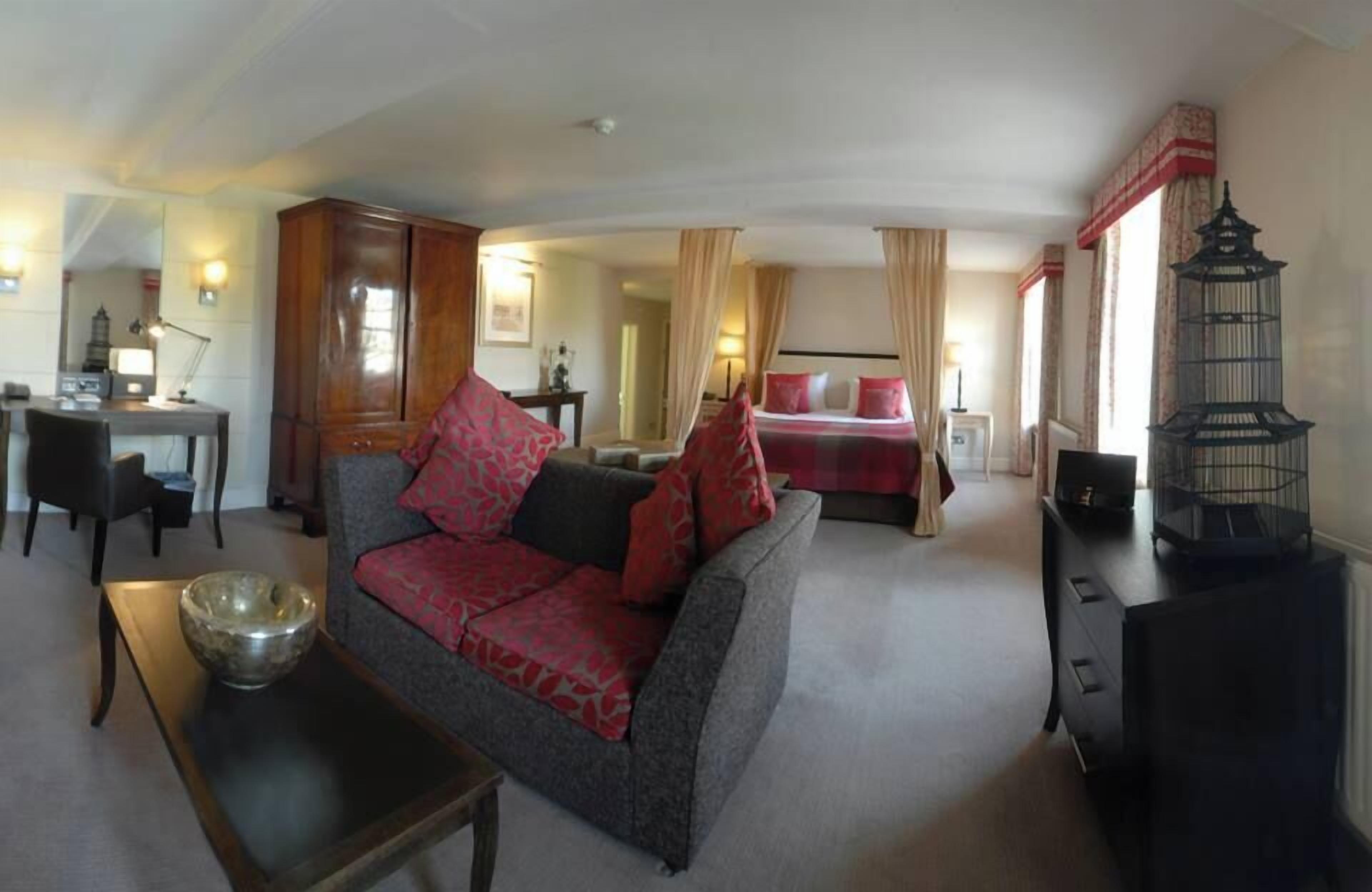 Una sala de estar con sofá, mesa de comedor, cama con cortinas, lámpara y una jaula decorativa.