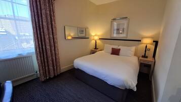 A hotel room with a large bed, two bedside tables with lamps, a window with curtains, and a framed picture on the wall.