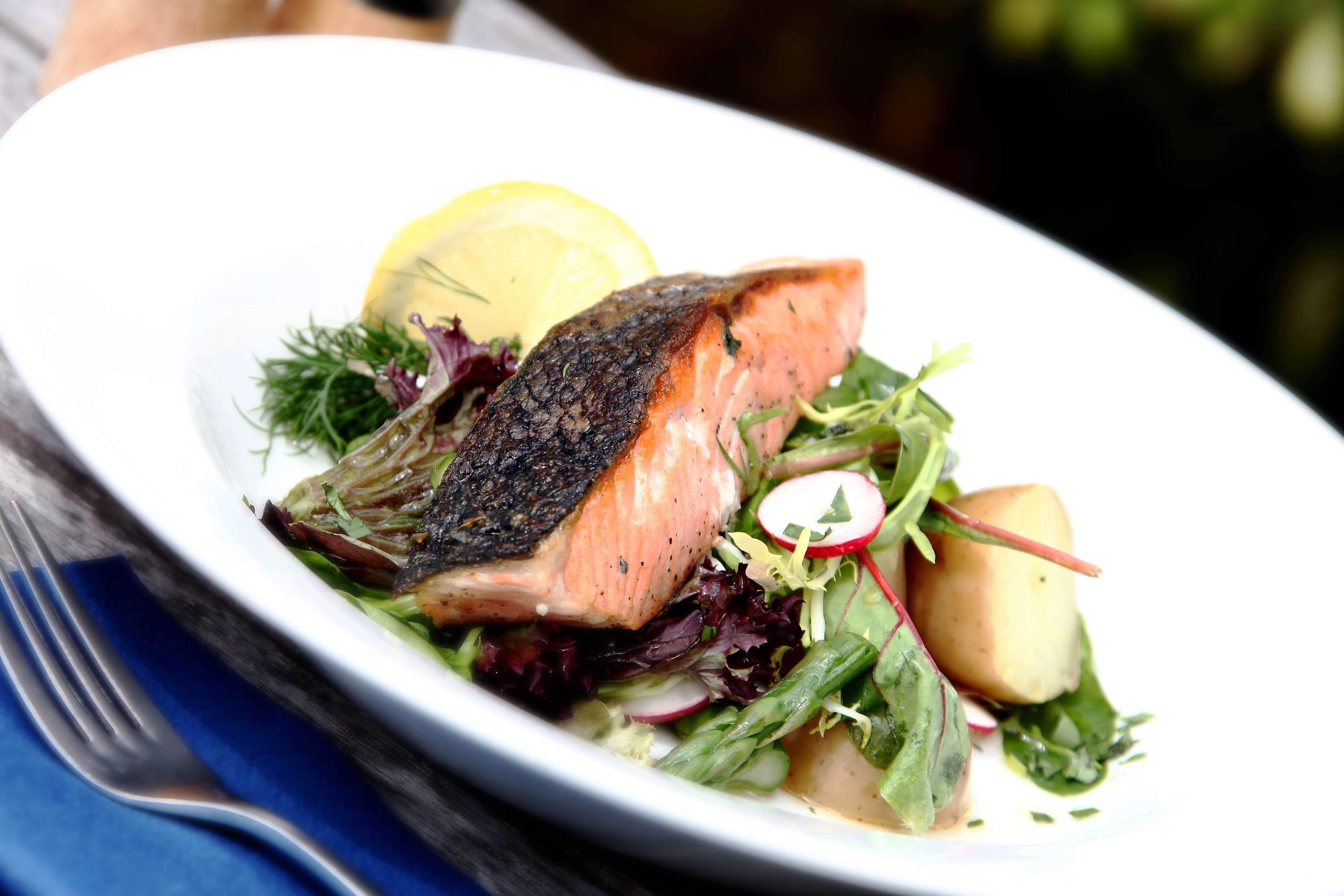 A plate of food with salmon, greens, and a lemon wedge.