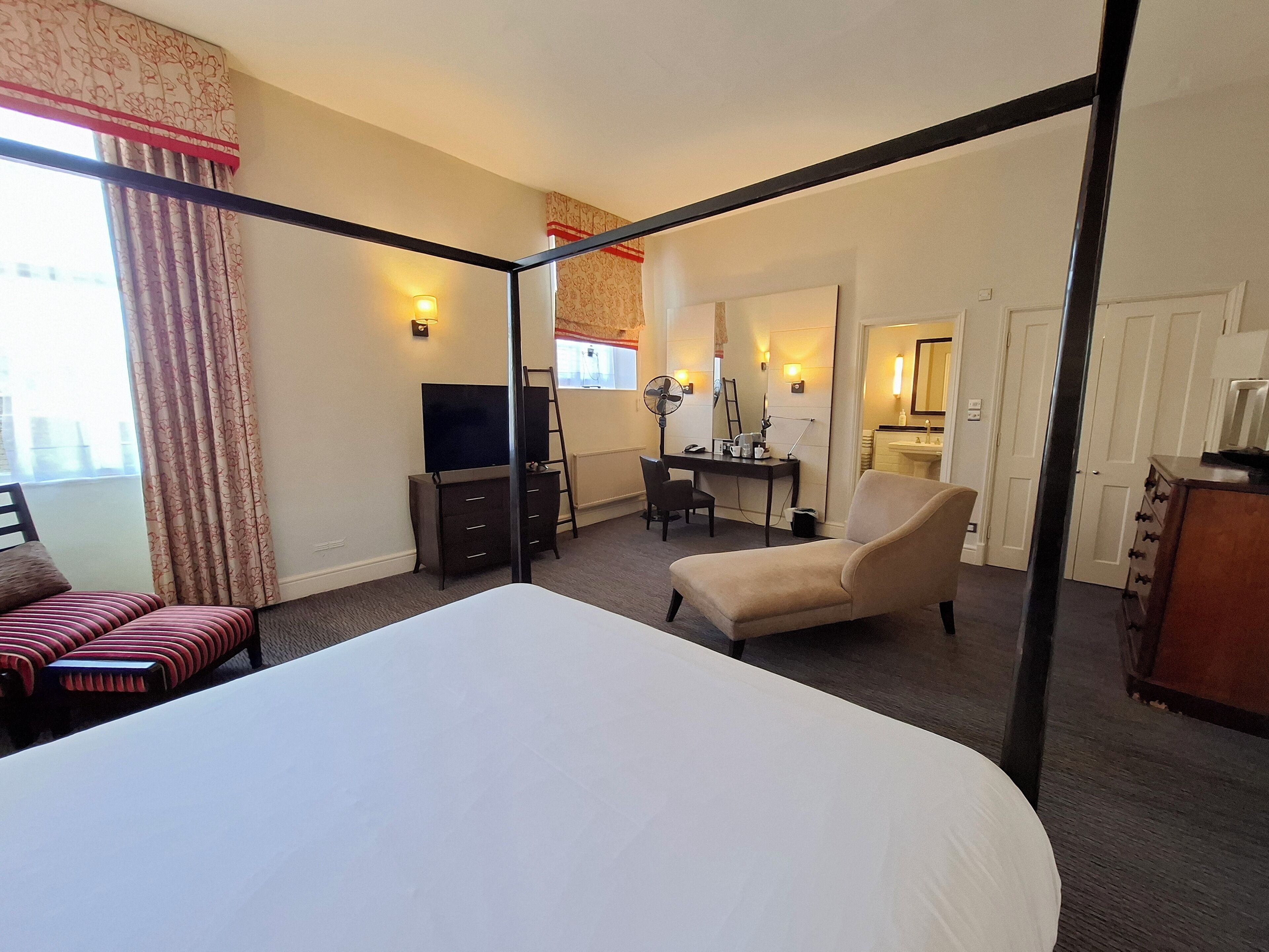 A hotel room with a large bed, a desk with a computer, a chair, a TV, and a bathroom with a sink and mirror.