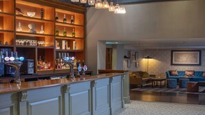A bar area with shelves of bottles and glasses, a bar counter with taps, and a seating area with sofas and a rug. - Best Western Plus Angel Hotel (Chippenham)