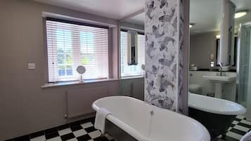 Een badkamer met een geruite vloer, een witte badkuip, een grote spiegel en een raam met jaloezieën.
