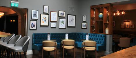 Un restaurante con un sofá tapizado en azul, mesas redondas y obras de arte enmarcadas en las paredes.