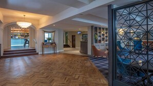 A spacious lobby with a wooden herringbone floor, a bar area with shelves, and a seating area with a geometric partition. - Best Western Plus Angel Hotel (Chippenham)