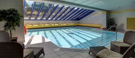 Una piscina interior con barrera de vidrio, rodeada de sillones de mimbre y una planta en maceta.