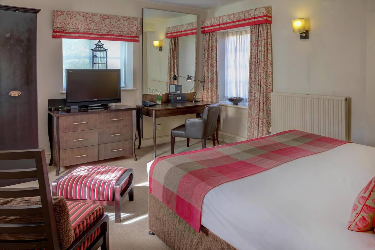 A hotel room with a bed, a desk with a computer, a chair, a television, and a wardrobe.