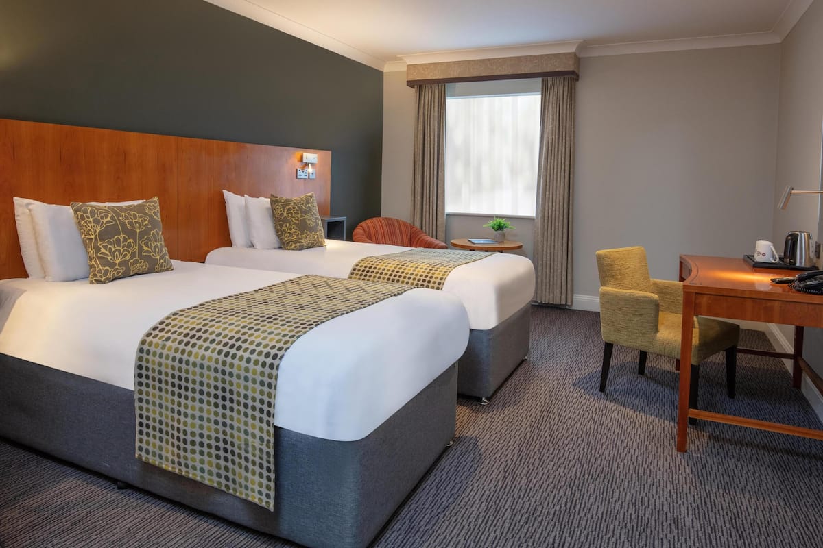 A hotel room with two beds, a desk, a chair, a small table, and a window with curtains.