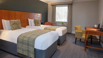 A hotel room with two beds, a desk, a chair, a small table, and a window with curtains.
