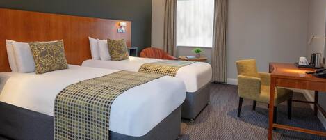 A hotel room with two beds, a desk, a chair, a small table, and a window with curtains.