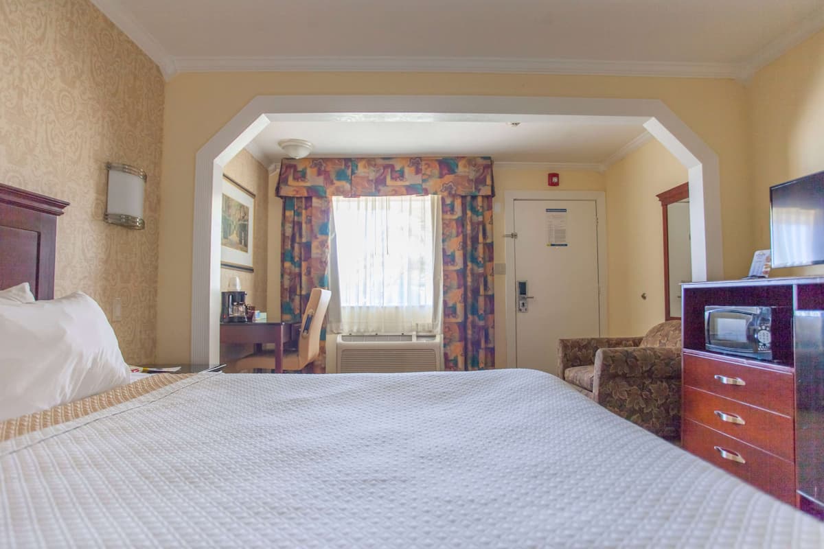 Une chambre d’hôtel avec un grand lit, un bureau avec une chaise, une télévision et une armoire.