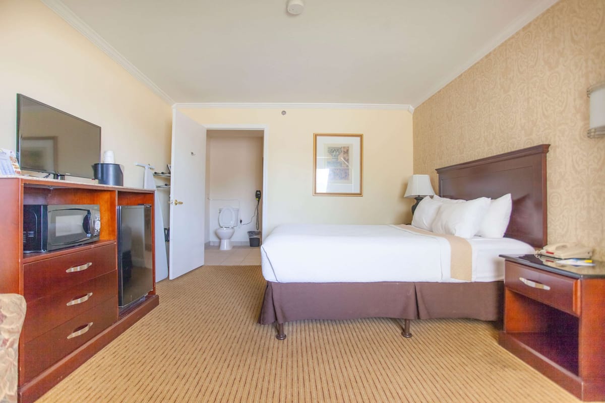 Une chambre d’hôtel comprenant un lit, un bureau avec un téléphone, un four à micro-ondes, un petit réfrigérateur et une salle de bain visible à travers une porte ouverte.