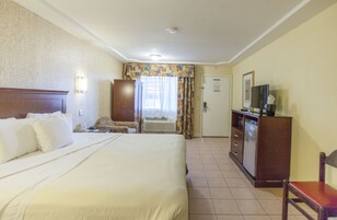 Habitación de hotel con una cama grande, un escritorio con televisor, un armario y una puerta que da a otra habitación.