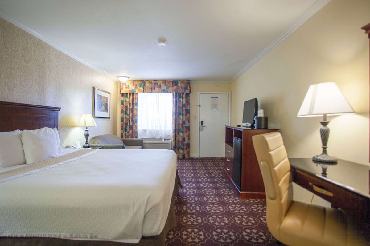 Une chambre d’hôtel avec un grand lit, un bureau avec une chaise, une télévision et une lampe de bureau.