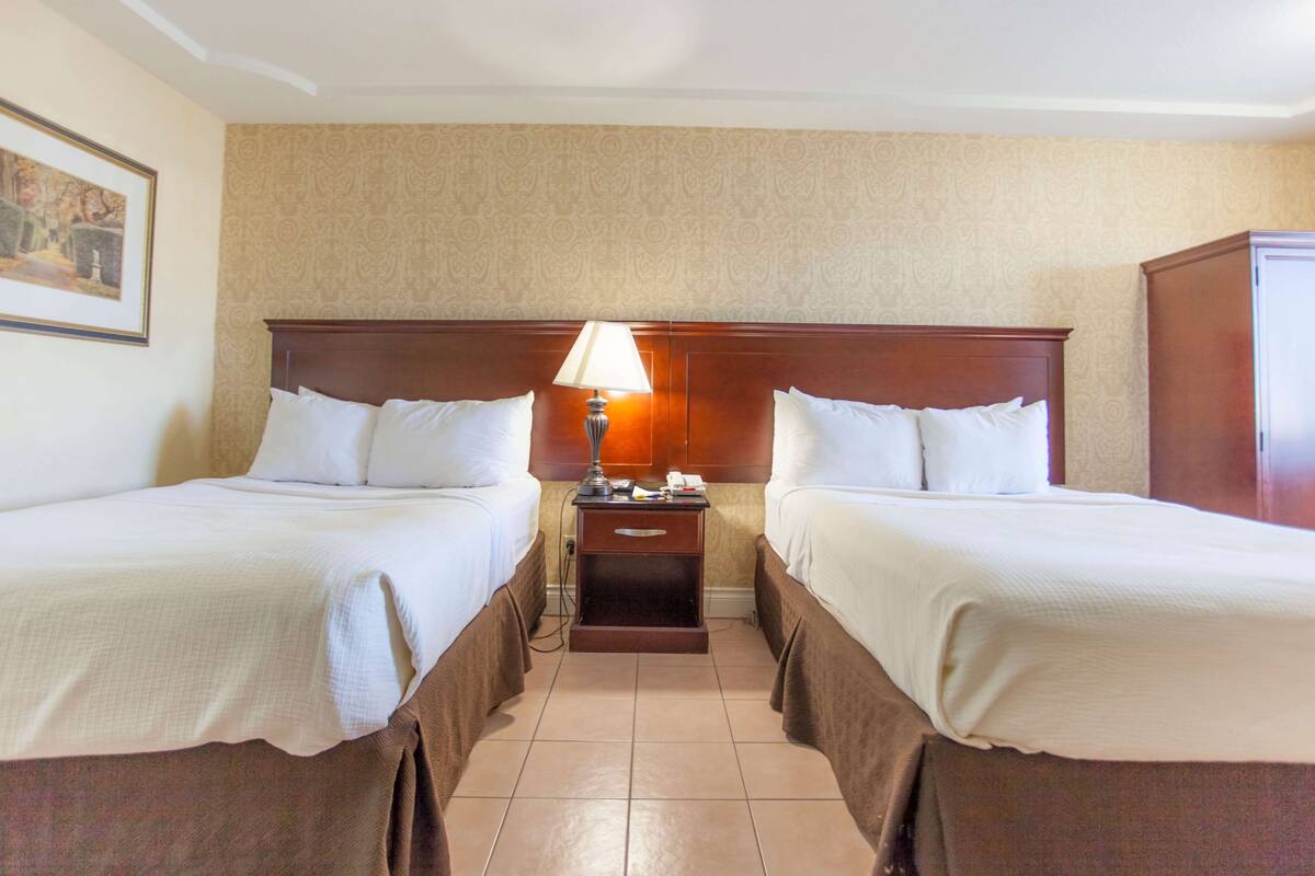 Une chambre d’hôtel avec deux lits, une table de chevet avec une lampe et une armoire.