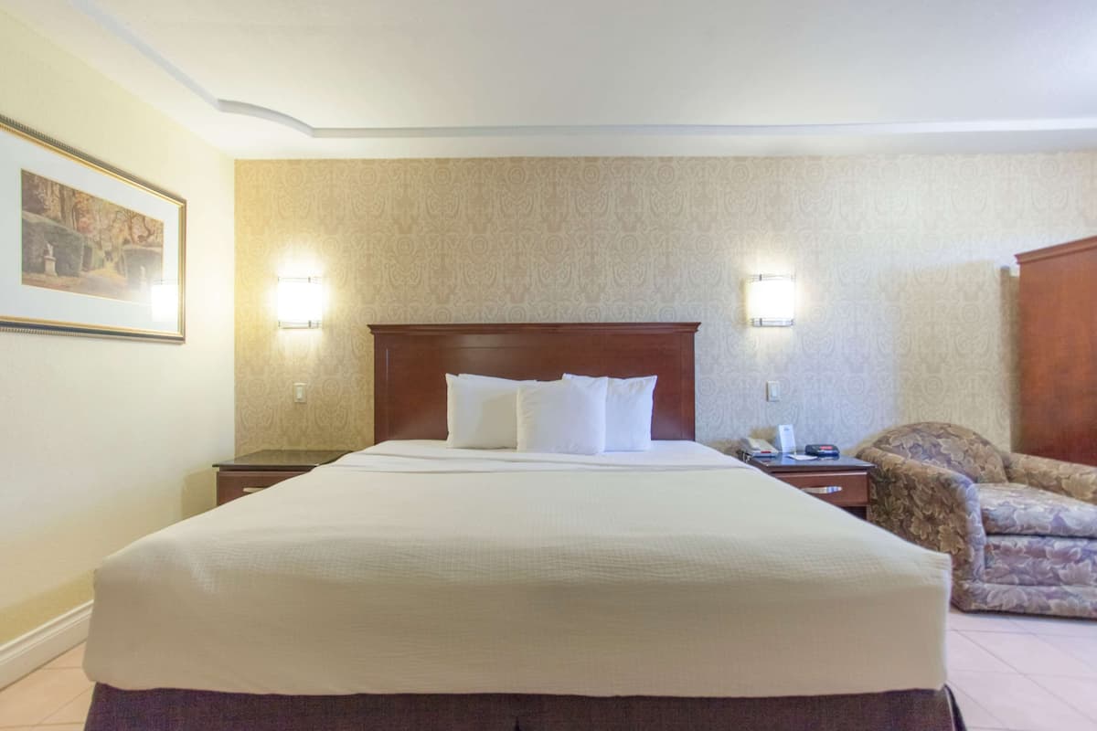 Une chambre d’hôtel avec un grand lit, deux lampes de chevet, une chaise et un tableau encadré au mur.