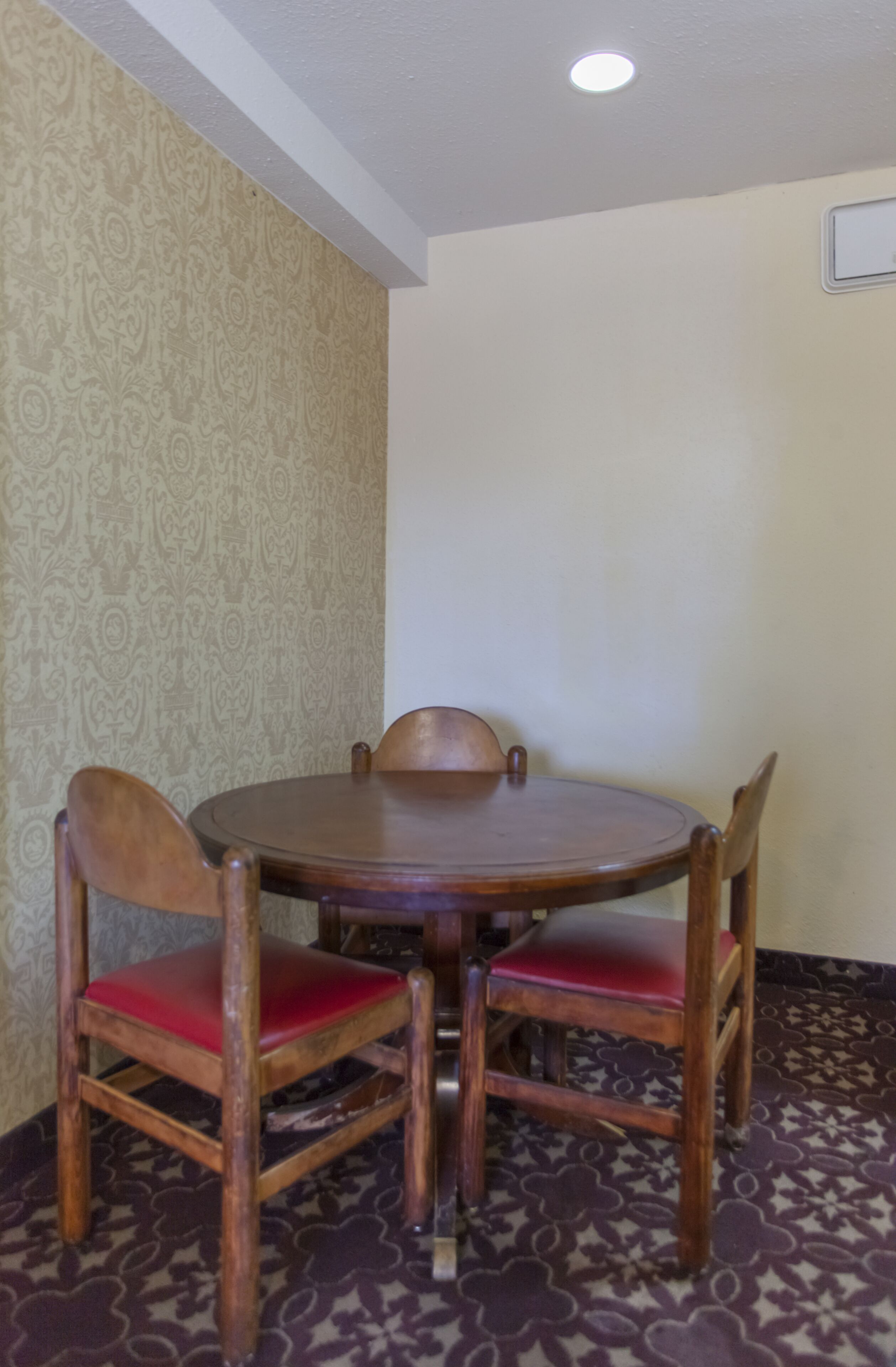A dining area with a round wooden table and four wooden chairs with red cushions.