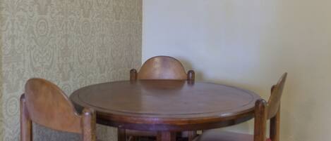 A dining area with a round wooden table and four wooden chairs with red cushions.