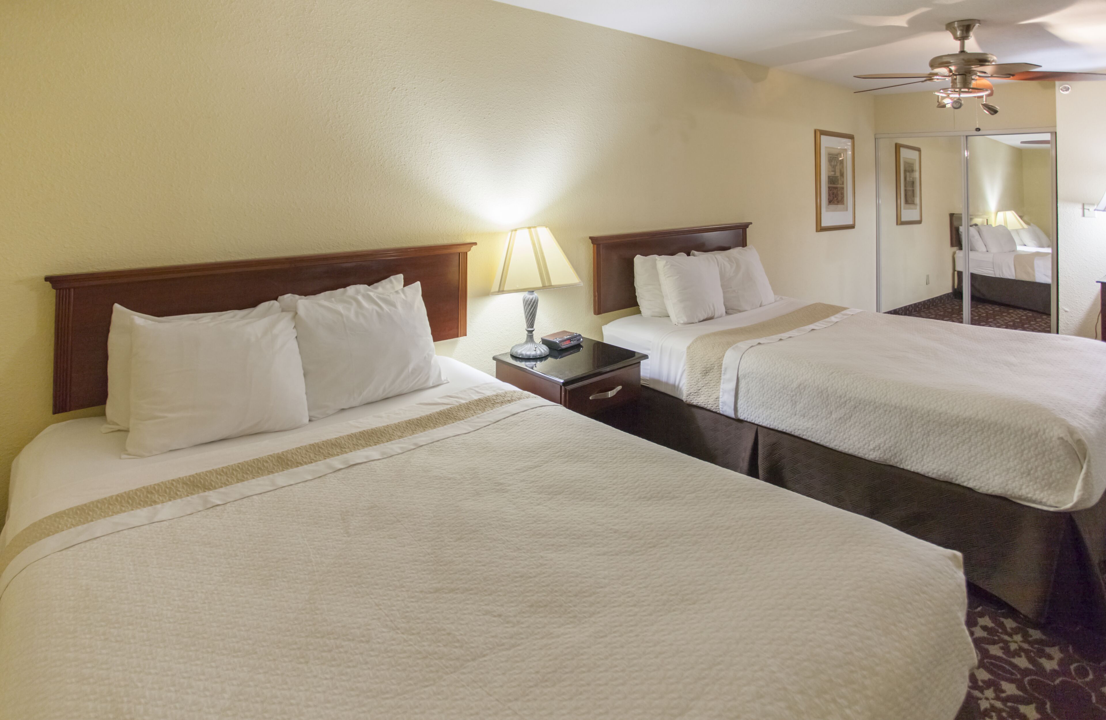 A hotel room with two beds, a nightstand, a lamp, and a ceiling fan.