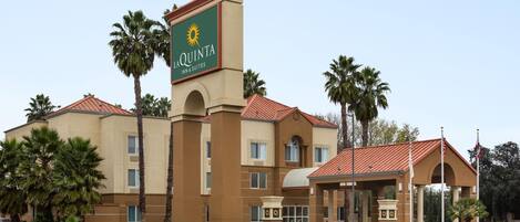 Edificio de La Quinta Inn & Suites con fachada color beige, techo de tejas rojas y palmeras.