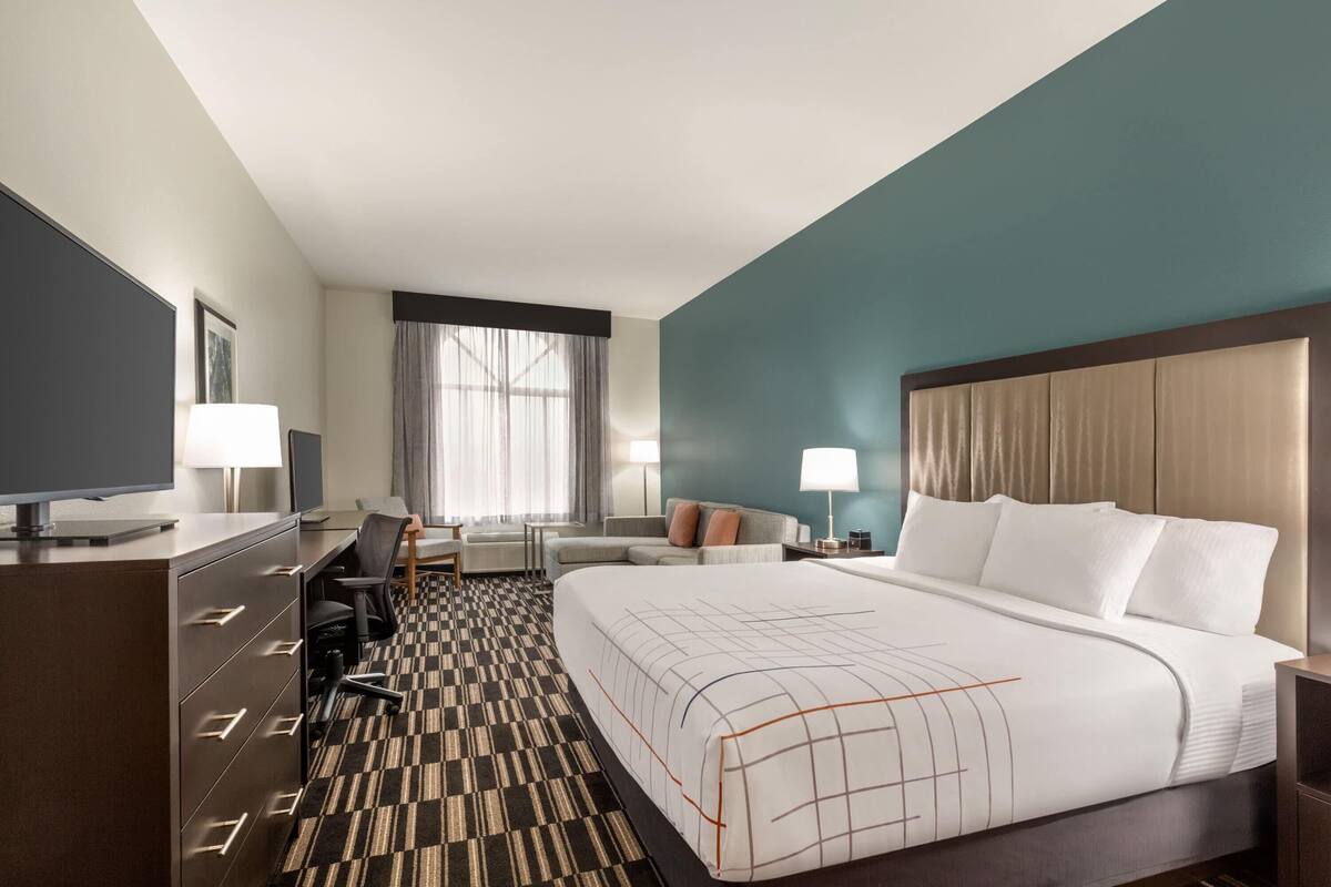 Ein Hotelzimmer mit einem großen Bett, einem Schreibtisch mit Stuhl, einem Fernseher und Blick ins Freie durch das Fenster.