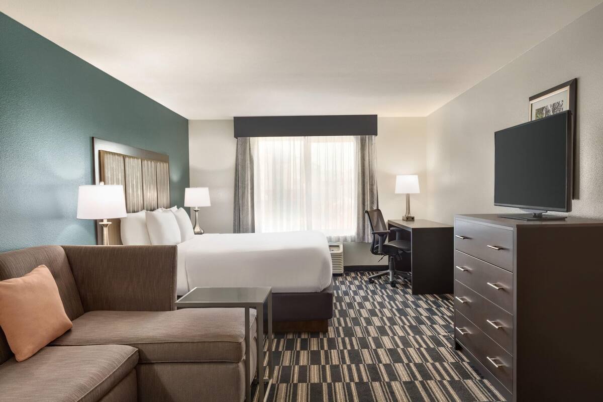 Ein Hotelzimmer mit Bett, einer Couch, einem Schreibtisch, einem Fernseher und einer Kommode.