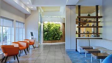 Een moderne lobby met een receptiebalie, een zithoek en een groene wand met planten.