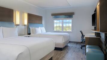 Quarto de hotel com duas camas, uma escrivaninha, uma cadeira, uma televisão e uma janela com vista.