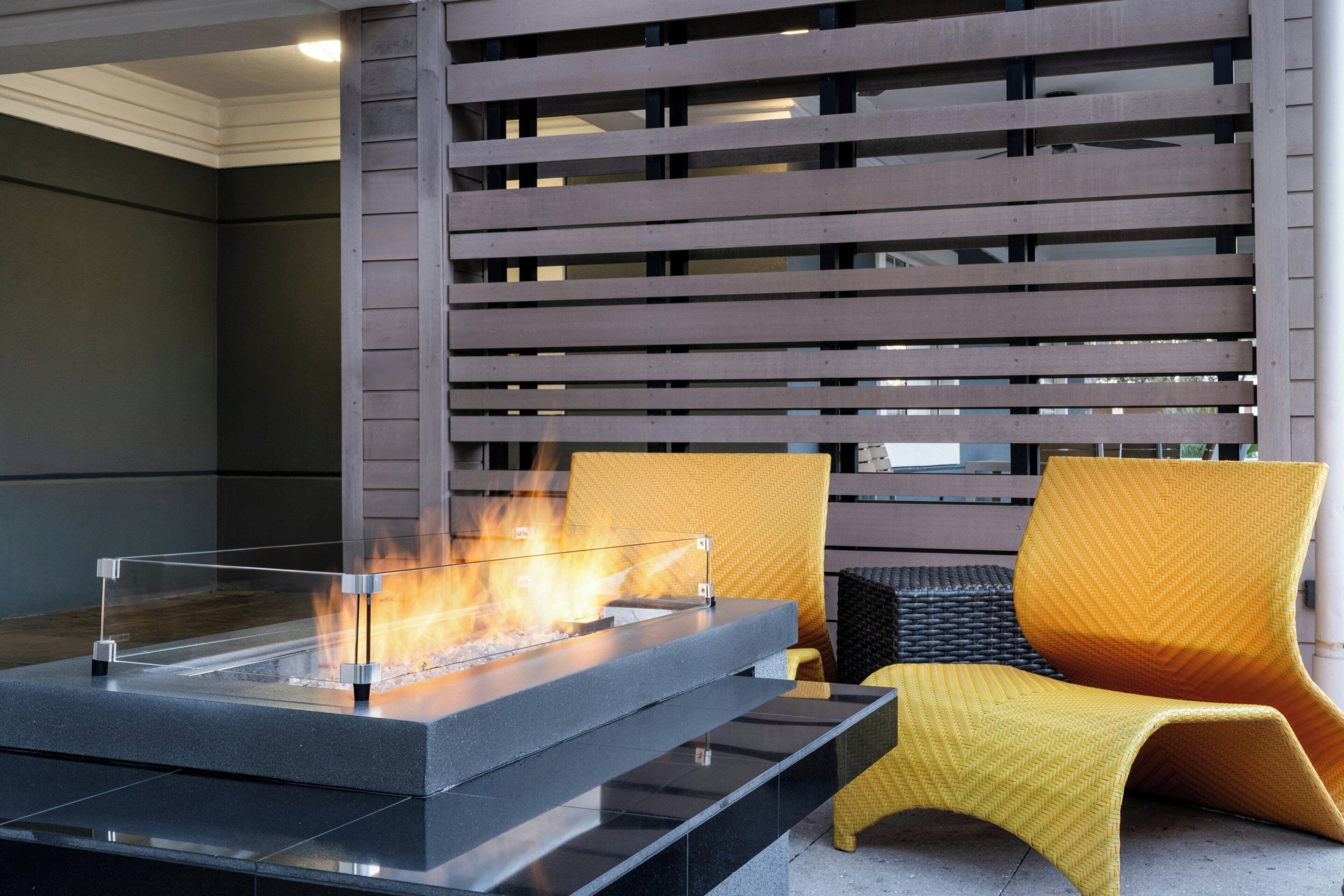 A modern outdoor seating area with a fire feature, a cushioned chair, and a wooden slatted wall.
