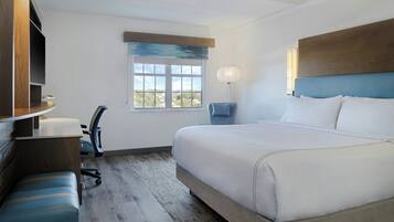 Habitación de hotel con una cama grande, un escritorio con una silla, una mesita, una lámpara y una ventana con vistas.