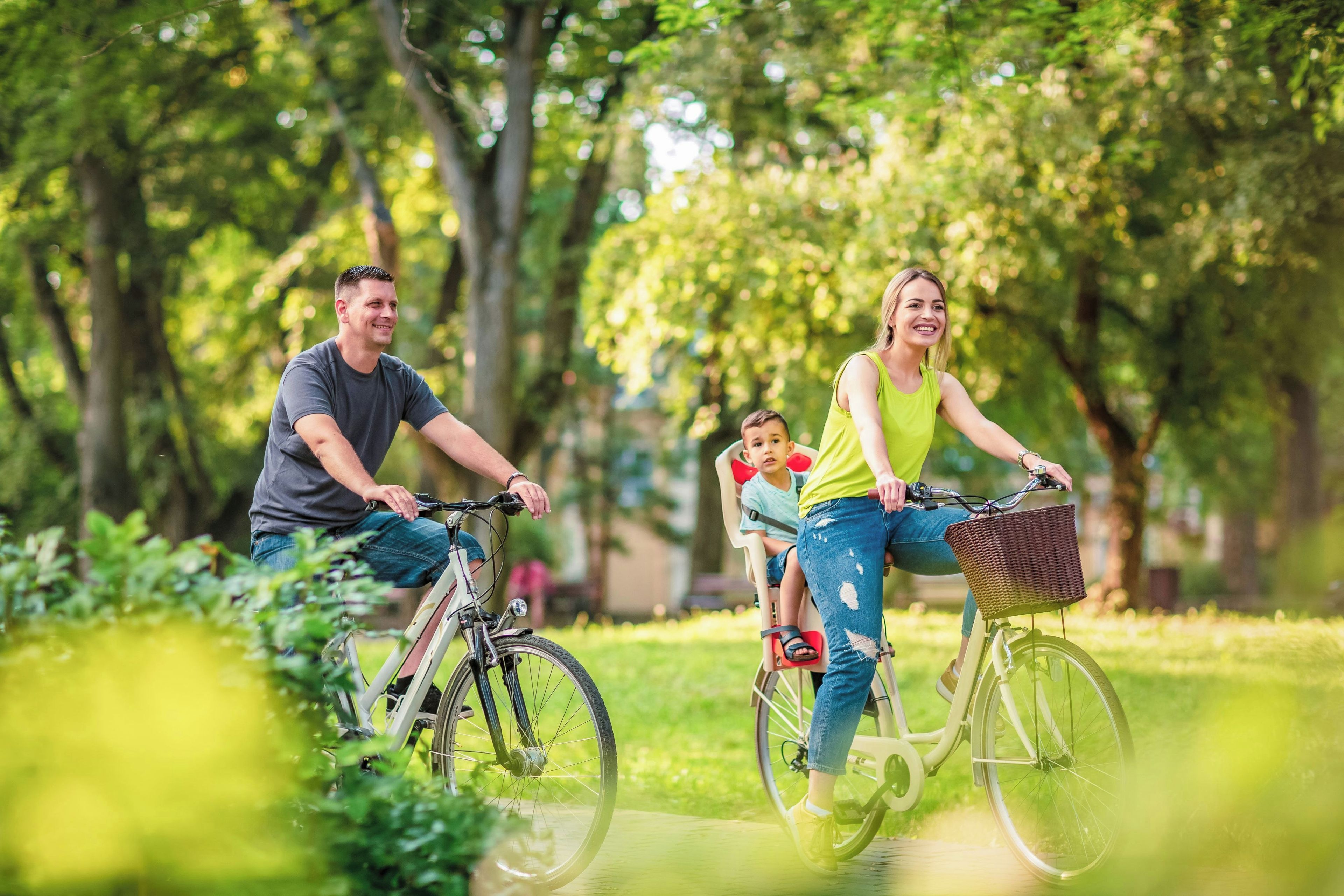 A family on bicycles in a park with trees and greenery.
