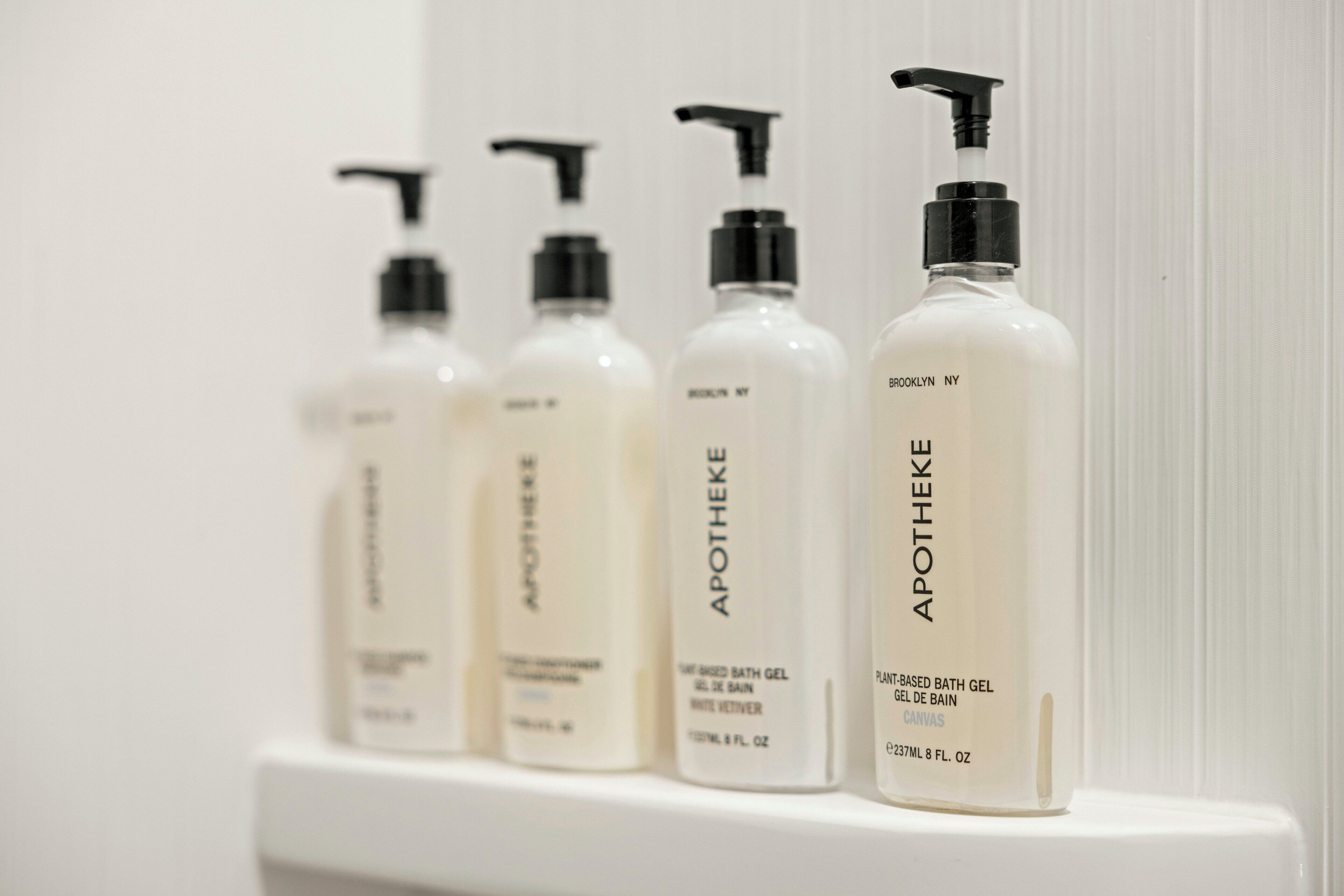 Cuatro botellas de gel de baño sobre un estante blanco.
