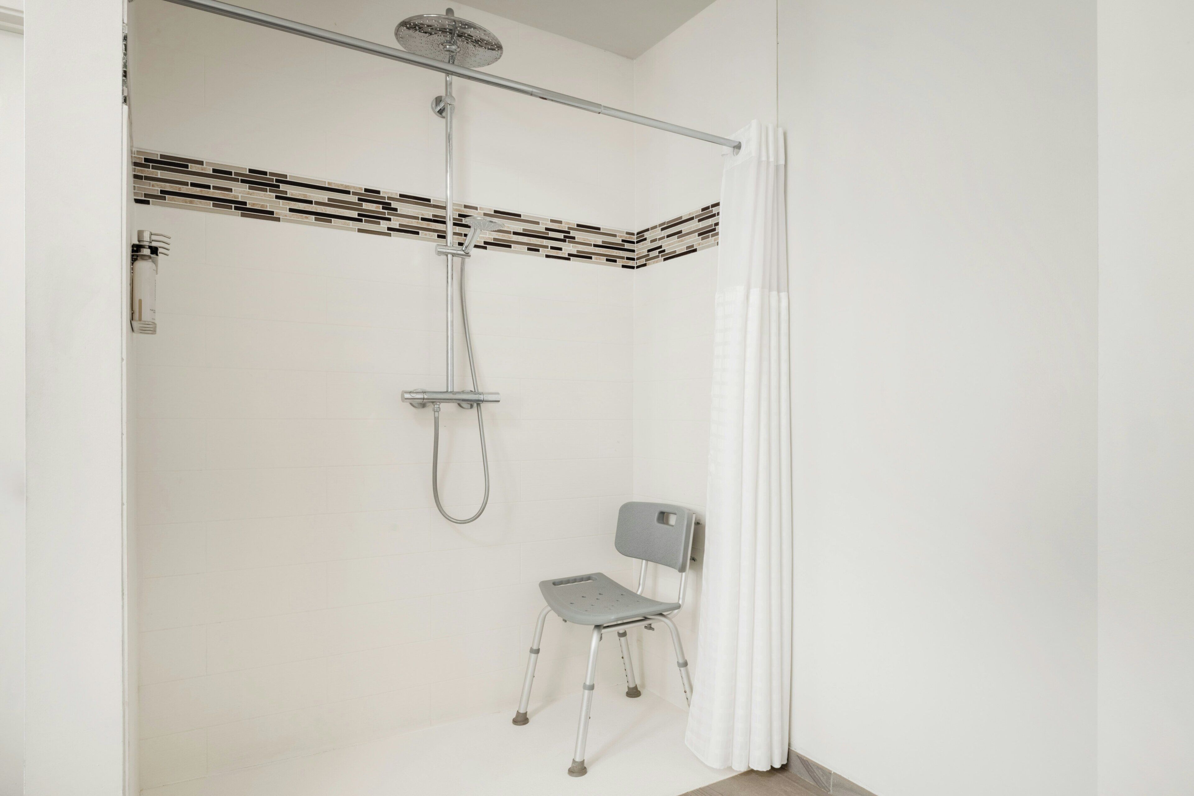 A shower area with a handheld showerhead, a handheld shower attachment, and a shower chair.