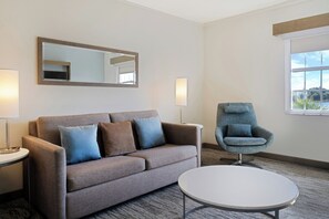 Une chambre d’hôtel avec un canapé, un fauteuil, une petite table et une fenêtre donnant sur un beau paysage.