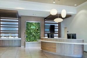 Un espace d’accueil moderne avec un comptoir de réception en bois, un jardin vertical verdoyant et des luminaires suspendus.