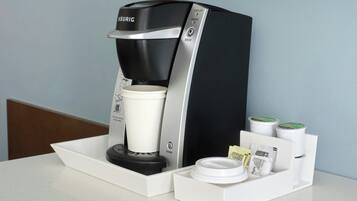 A Keurig coffee maker with a cup holder, a power button, and a tray with a cup and coffee pods.