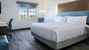 A hotel room with a large bed, a desk, a chair, a lamp, and a window with a view.