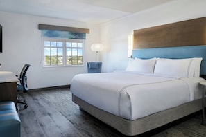 A hotel room with a large bed, a desk, a chair, a lamp, and a window with a view.