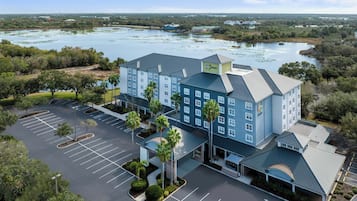 A hotel with a parking lot, a lake, and surrounding greenery.