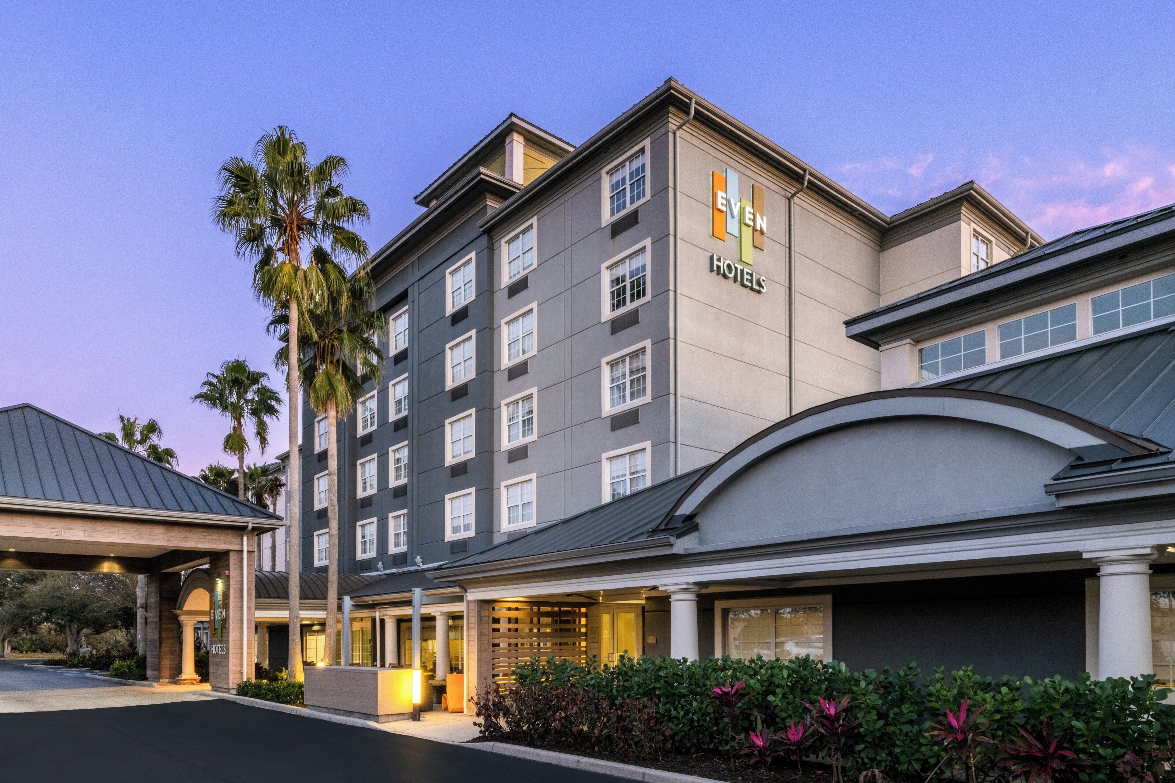 A multi-story hotel building with a modern architectural design, featuring a prominent sign for 'Even Hotels' and a covered entrance area.