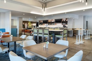 Un moderno vestíbulo de hotel con zona de bar, asientos y una pantalla de televisión.